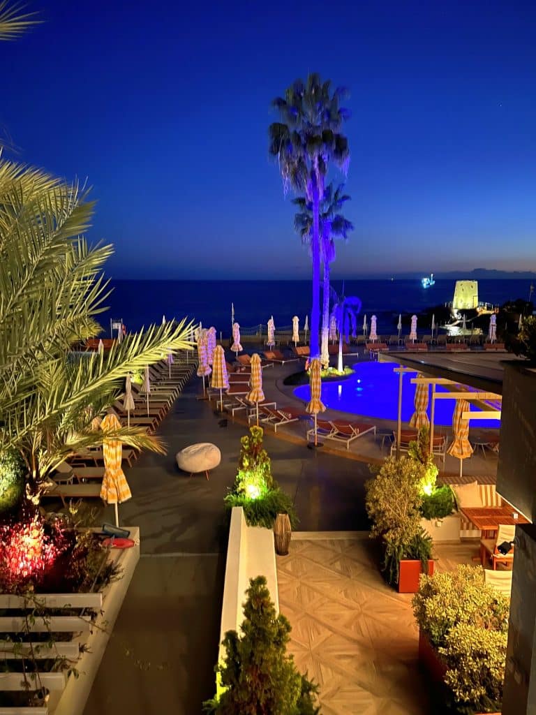 Taras z oświetlonym na niebiesko basenem i palmą w hotelu NEXT wieczorem, w tle ocean