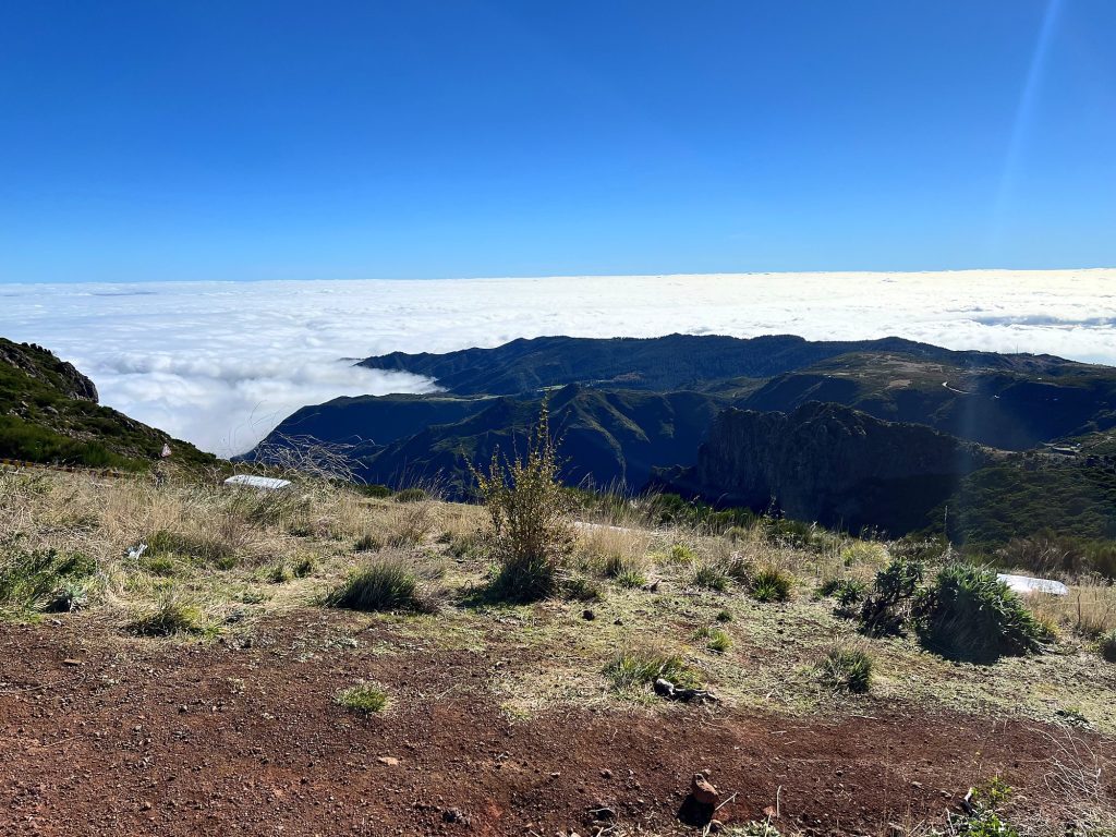 Morze chmur pod grzbietami gór przy Pico do Arieiro, na pierwszym planie czerwona ziemia i suche krzewy