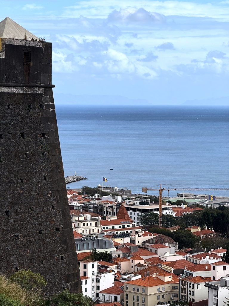 Ciemna kamienna wieża twierdzy Fortaleza do Pico nad dachami centrum Funchal i oceanem