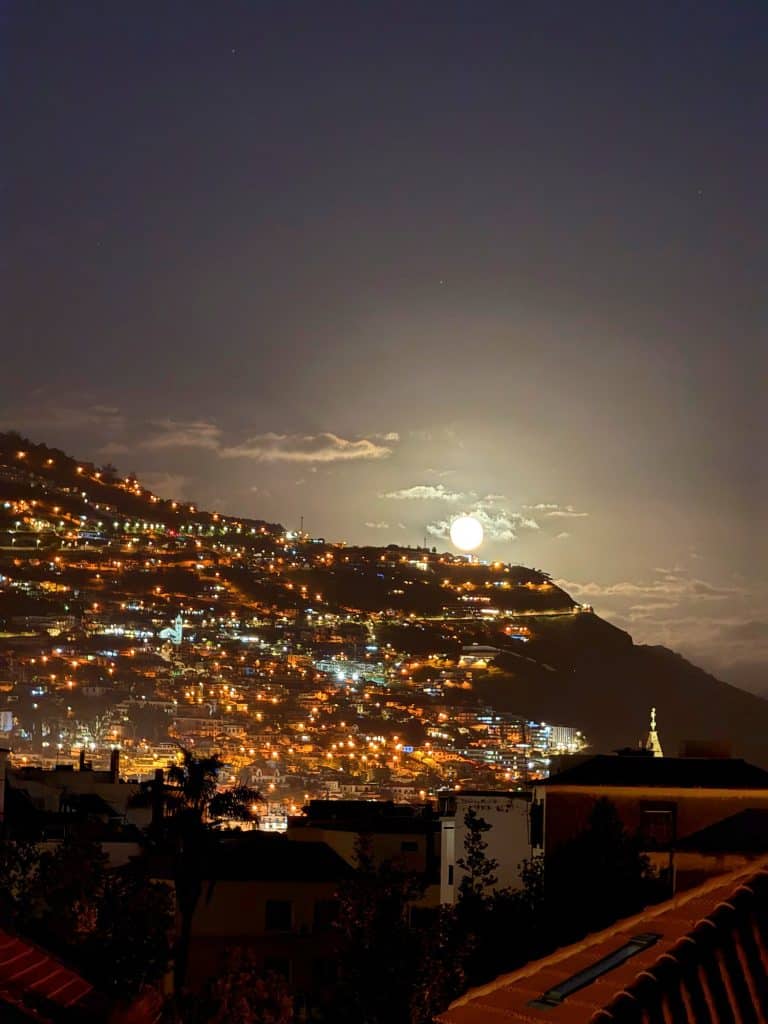 Księżyc w pełni nisko nad oświetlonym nocą zboczem Funchal, na pierwszym planie dachy