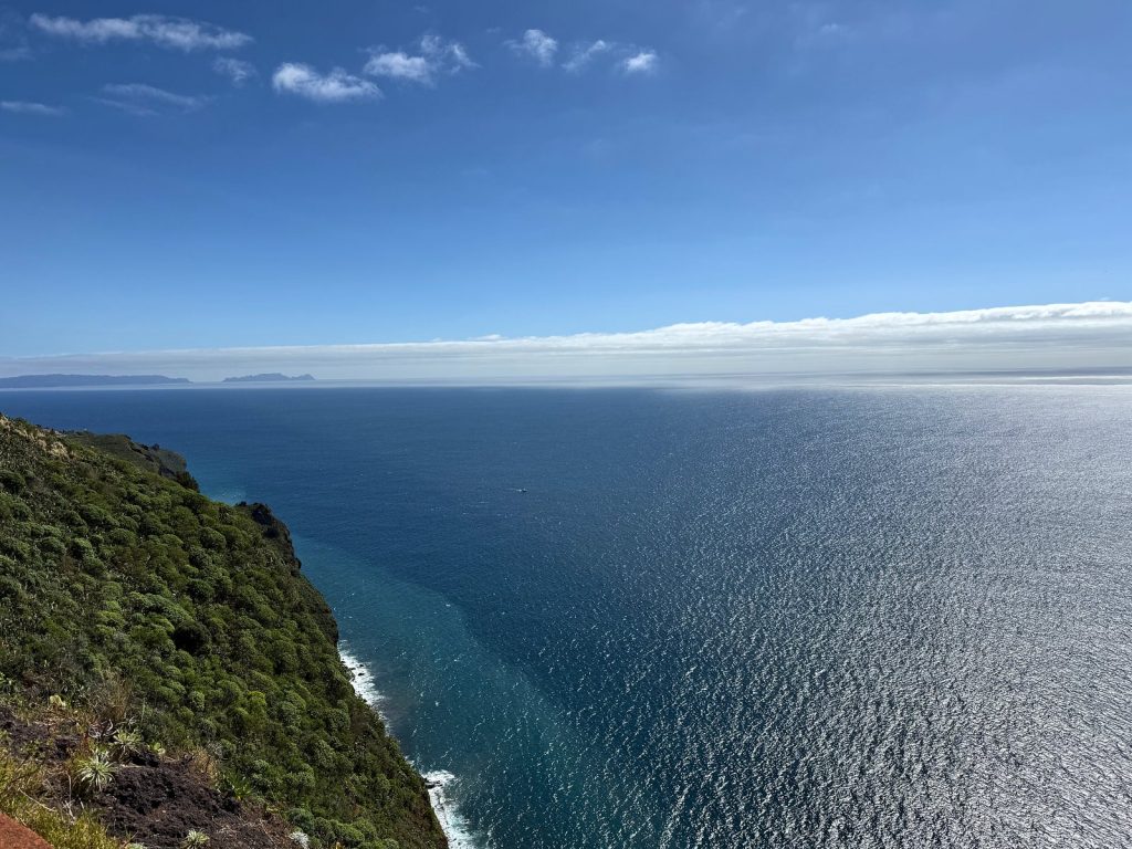 Zielone zbocze klifu opadające do oceanu, na horyzoncie pas chmur